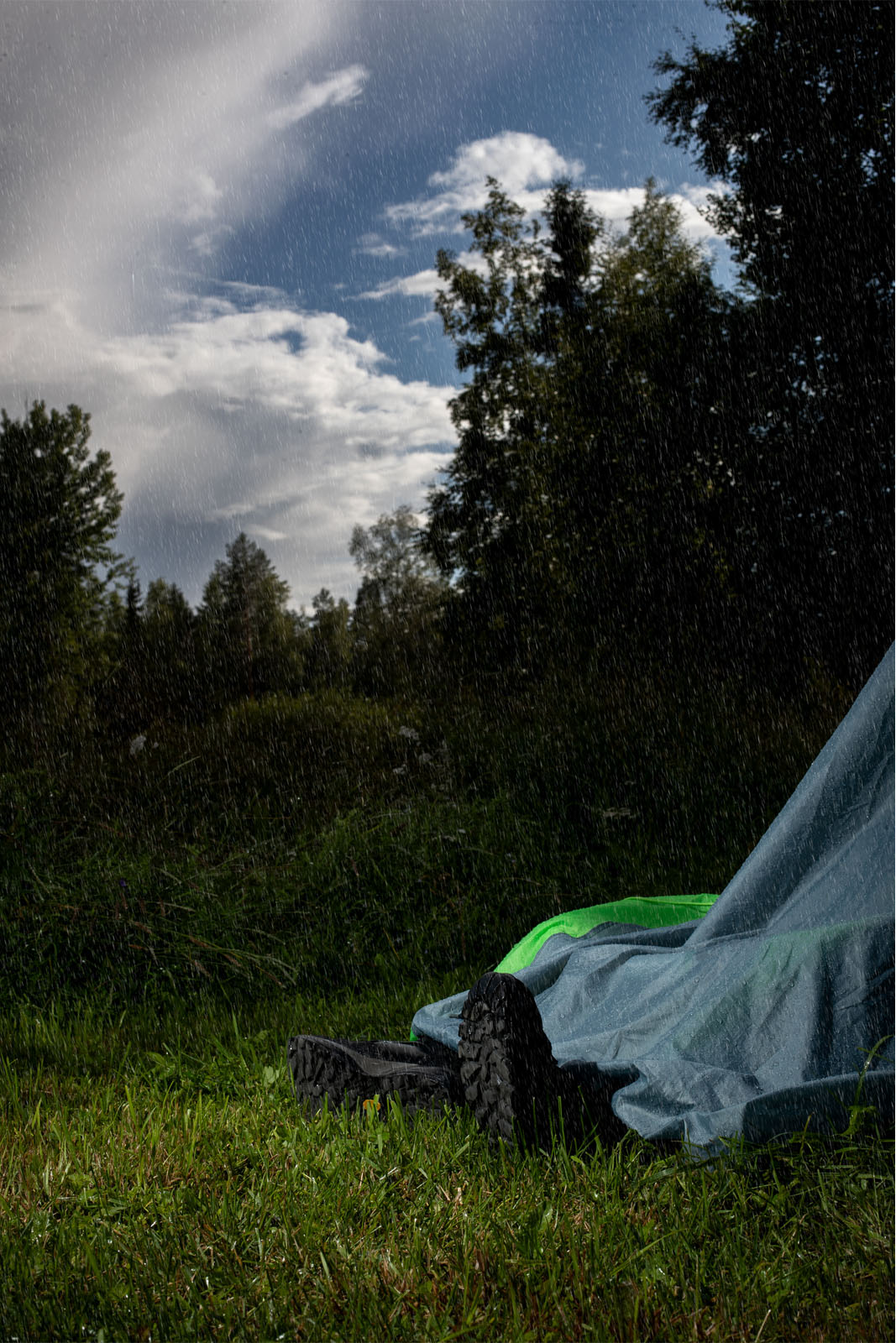 Man lays inside a collapsed tent while it's raining, only boots showing.