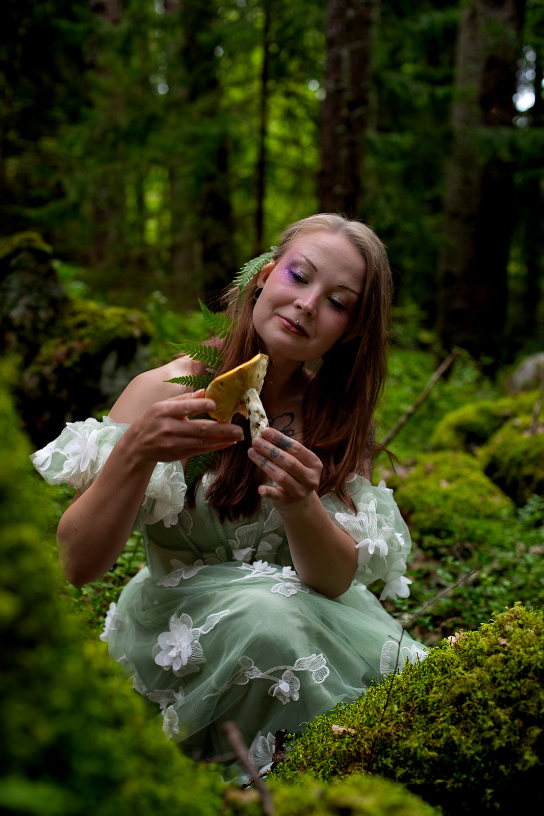 A fairy sits in forest, looking at a mushroom happily.